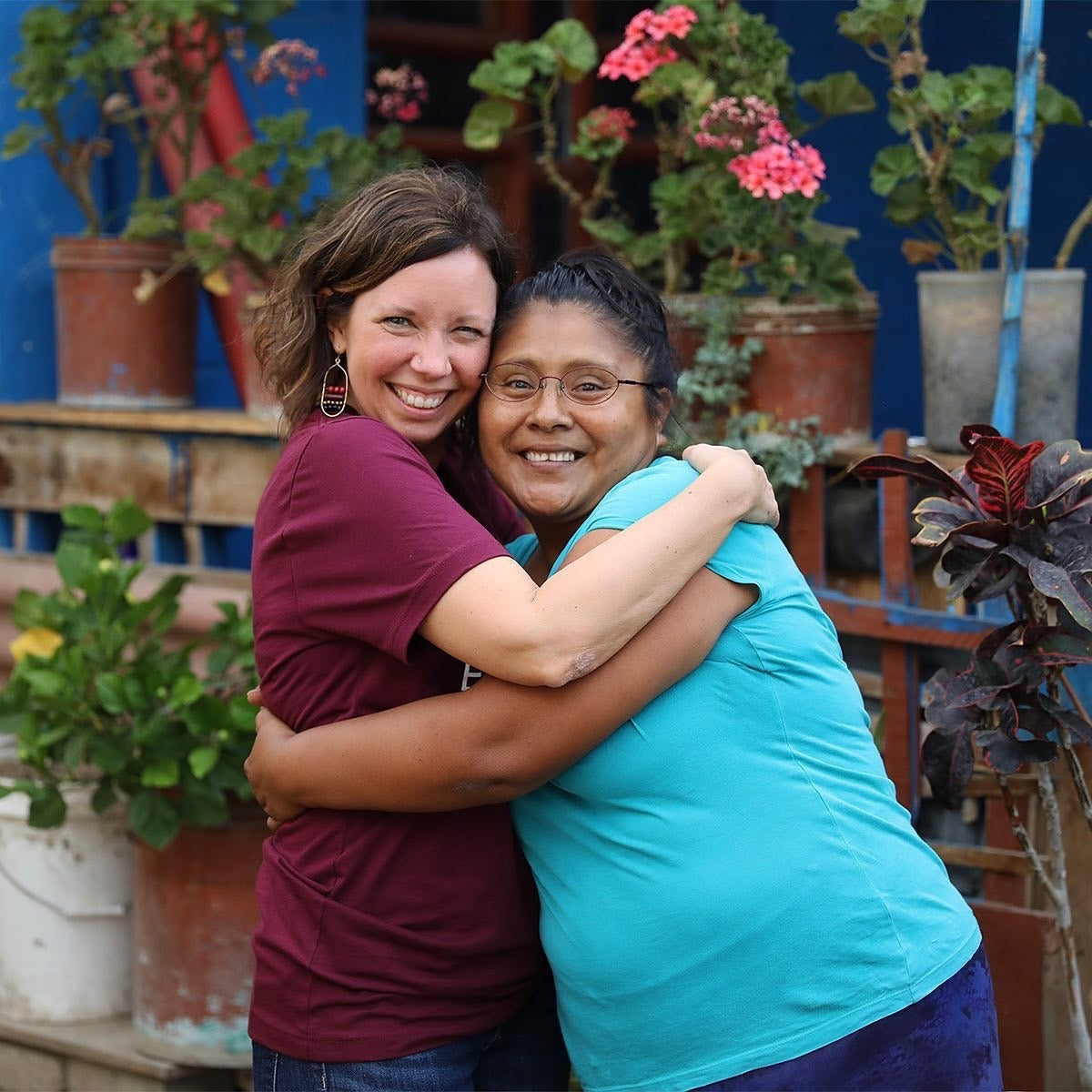 Two women hugging in front of potted plants